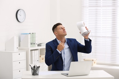 Photo of Man enjoying air flow from fan at workplace