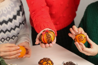 Photo of Friends decorating fresh tangerines with cloves at light wooden table, closeup. Making Christmas pomander balls