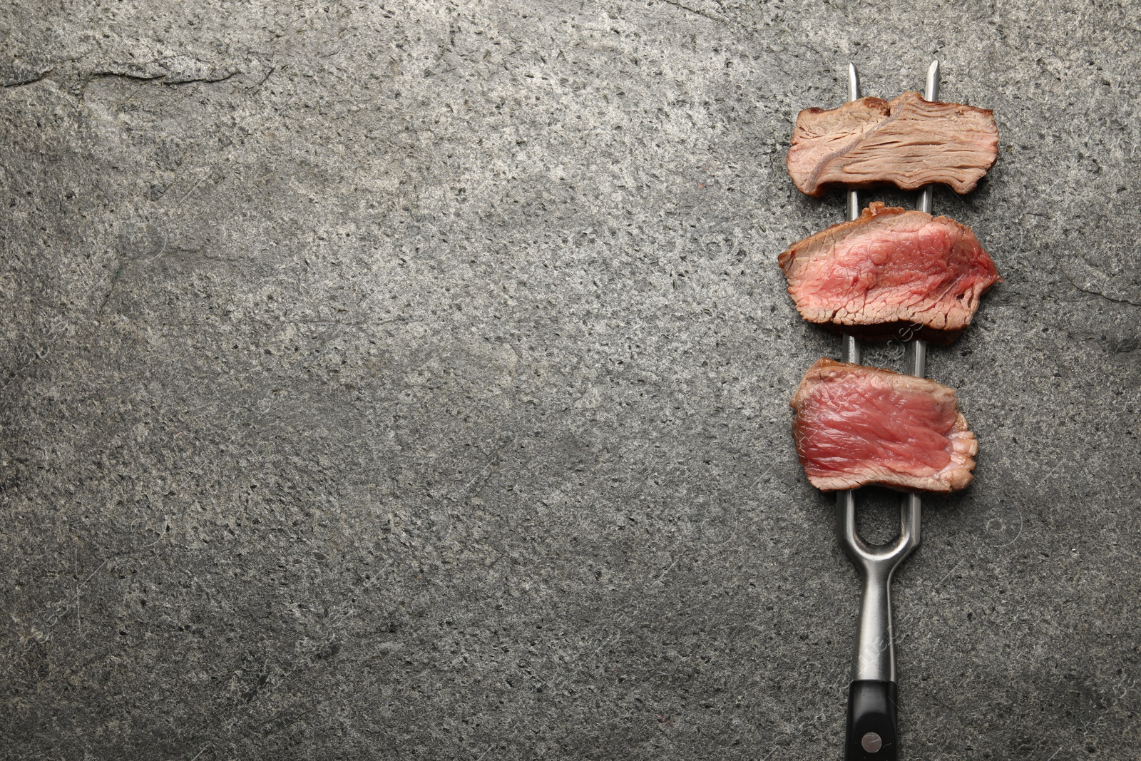 Photo of Delicious sliced beef tenderloin with different degrees of doneness on grey table, top view. Space for text