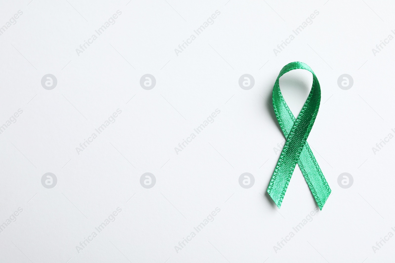 Photo of Green ribbon on white background, top view. Cancer awareness