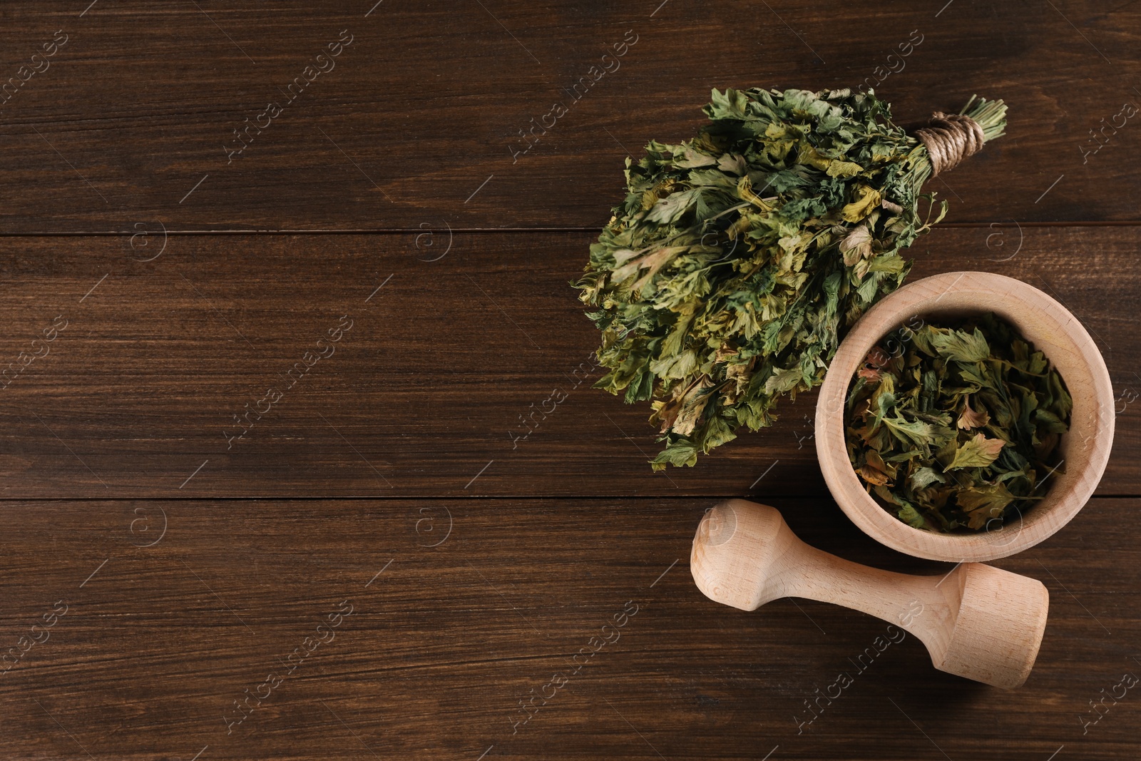 Photo of Mortar and pestle with dry parsley on wooden table, flat lay. Space for text