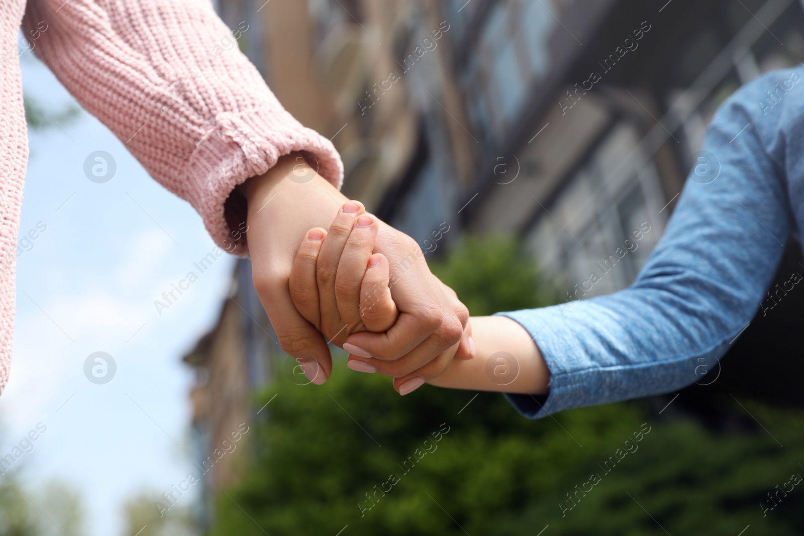 Photo of Little child holding hands with his mother outdoors, closeup. Family time