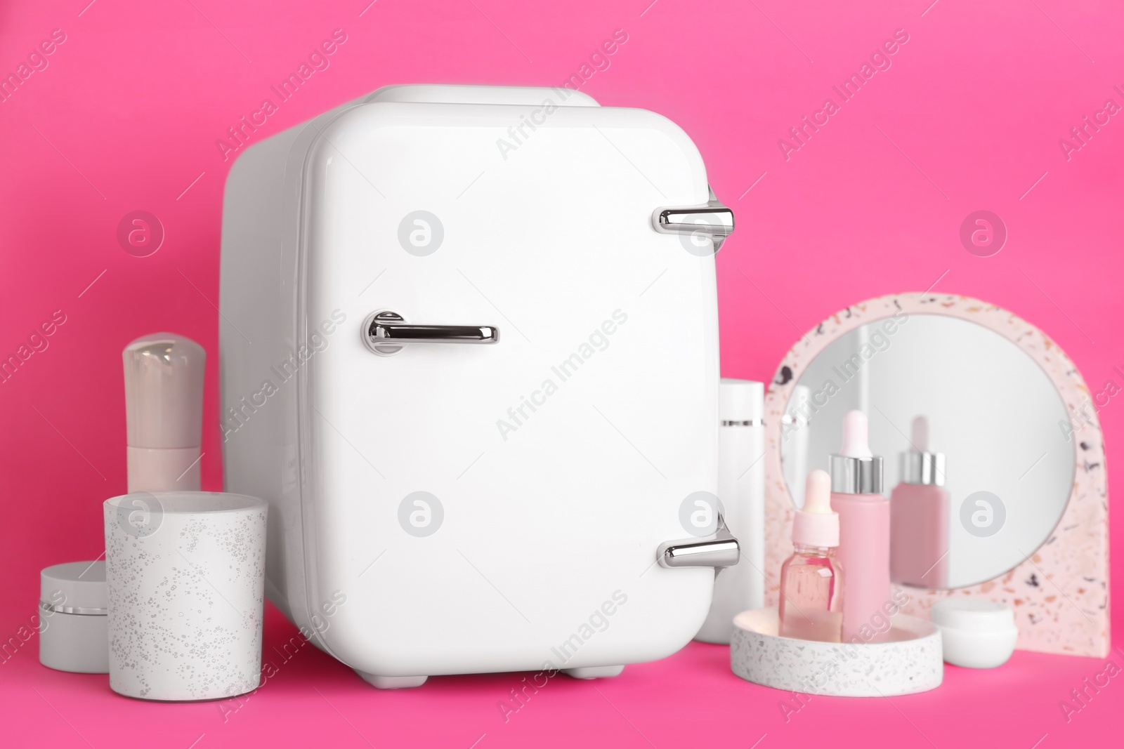 Photo of Cosmetic refrigerator and skin care products on pink background