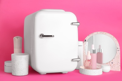 Photo of Cosmetic refrigerator and skin care products on pink background