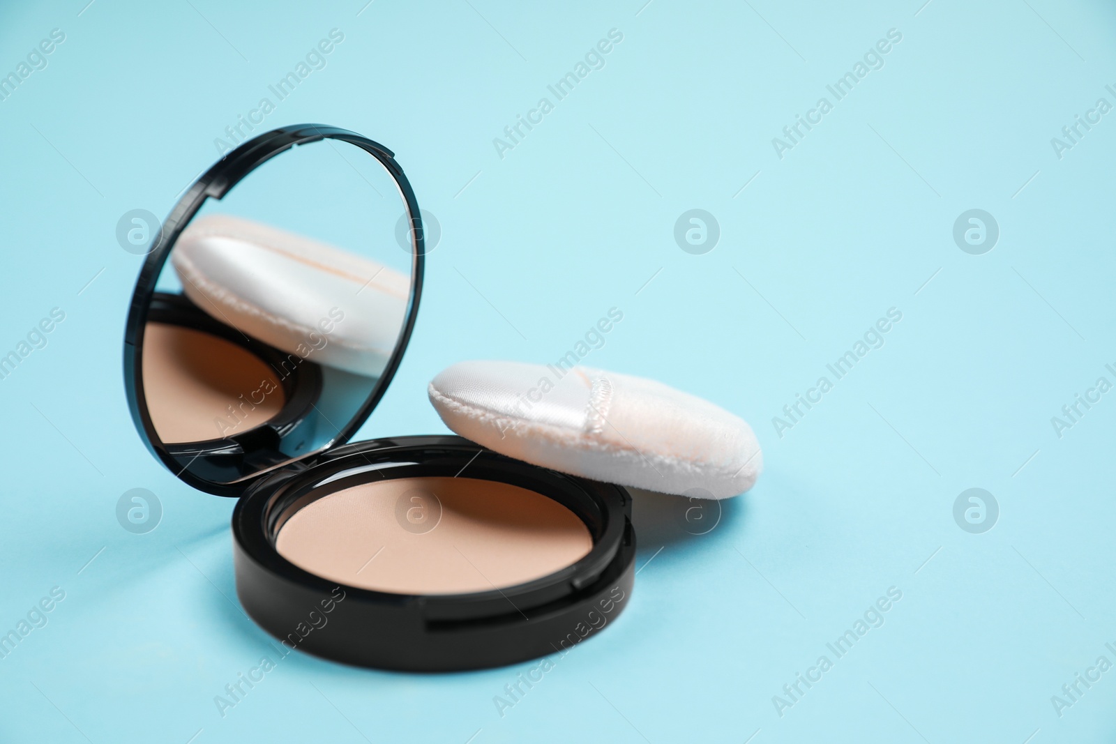 Photo of Face powder and puff on light blue background. Space for text