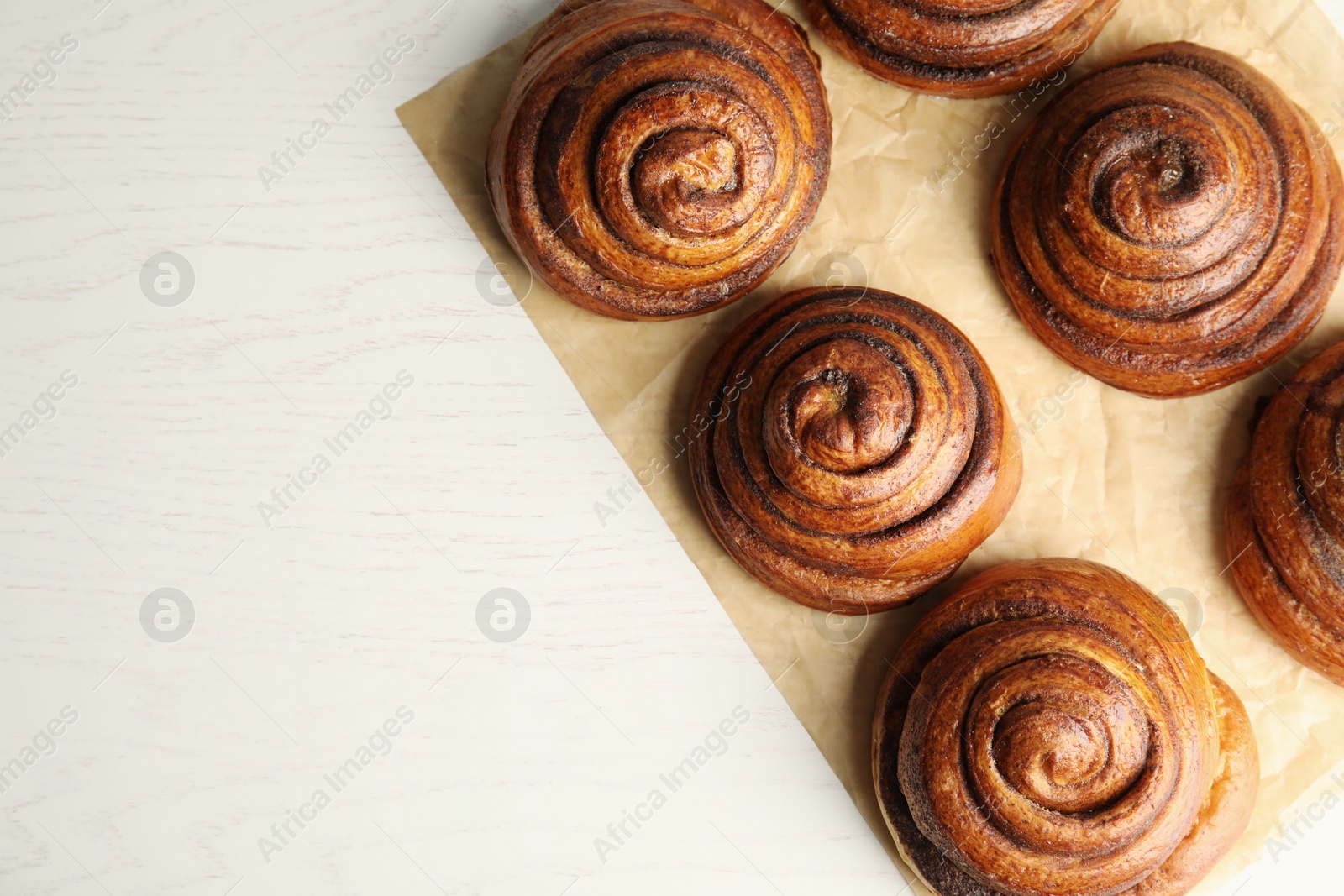 Photo of Parchment with cinnamon rolls on white wooden background, top view. Space for text