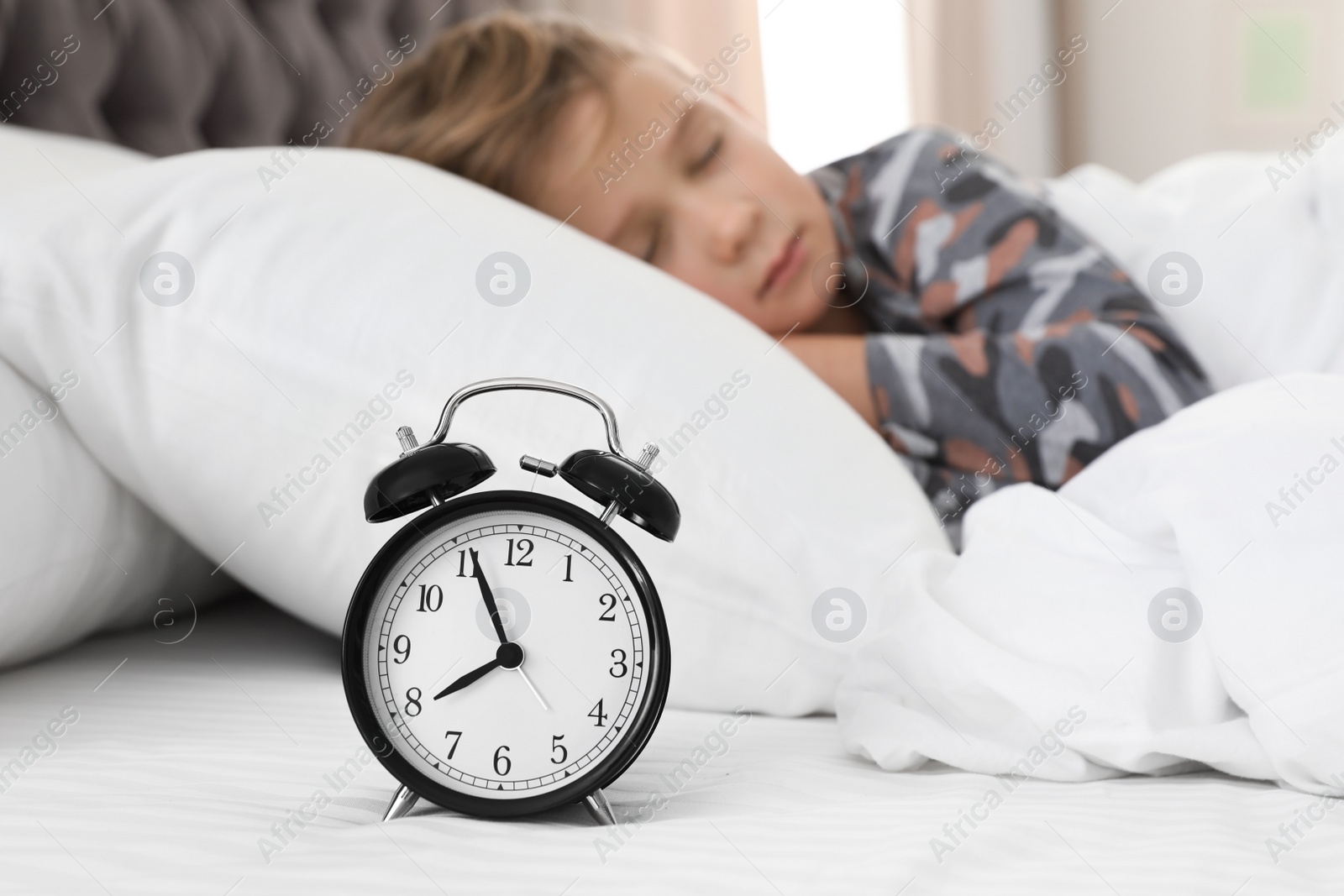 Photo of Cute boy with alarm clock sleeping in bed