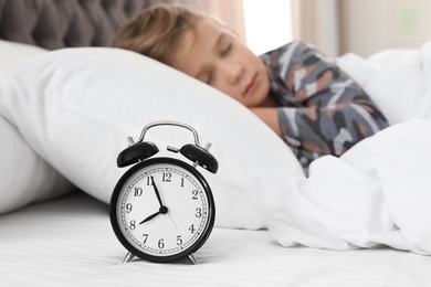 Photo of Cute boy with alarm clock sleeping in bed