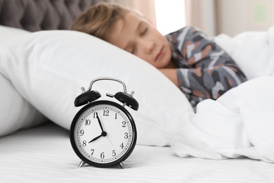 Cute boy with alarm clock sleeping in bed