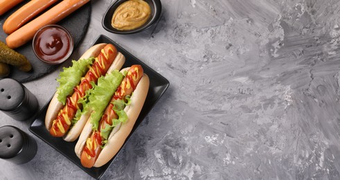 Photo of Tasty hot dogs and ingredients on grey textured table, flat lay. Space for text