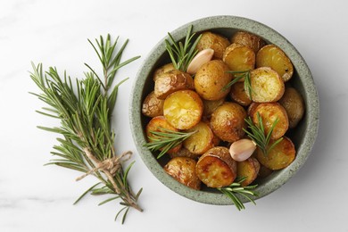 Tasty baked potato and aromatic rosemary on white marble table, flat lay