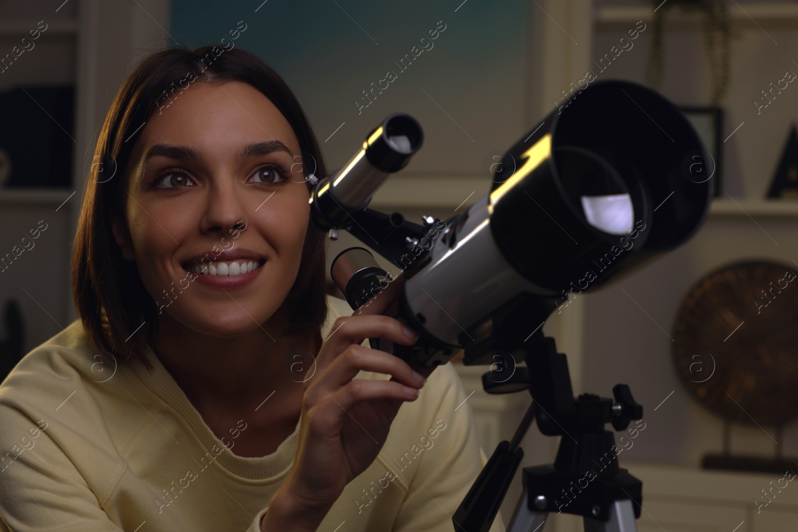 Photo of Beautiful young woman looking at stars through telescope in room