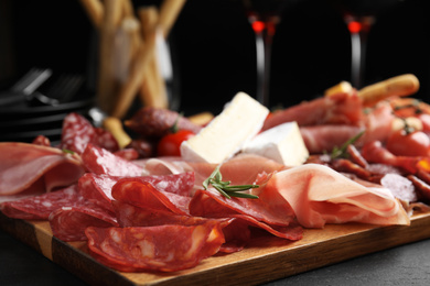 Photo of Tasty prosciutto with other delicacies served on black table, closeup