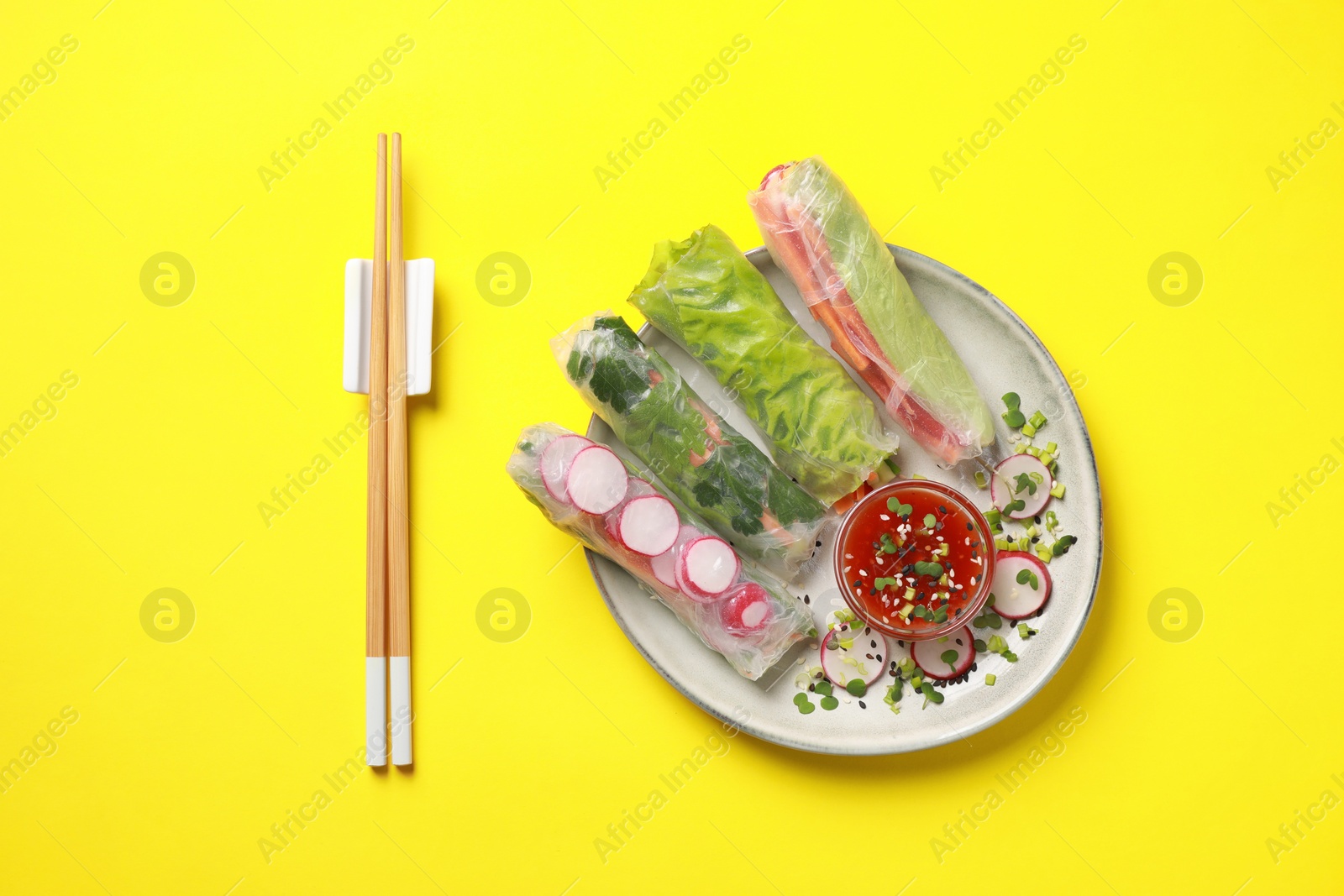 Photo of Delicious spring rolls served with sauce on yellow background, flat lay