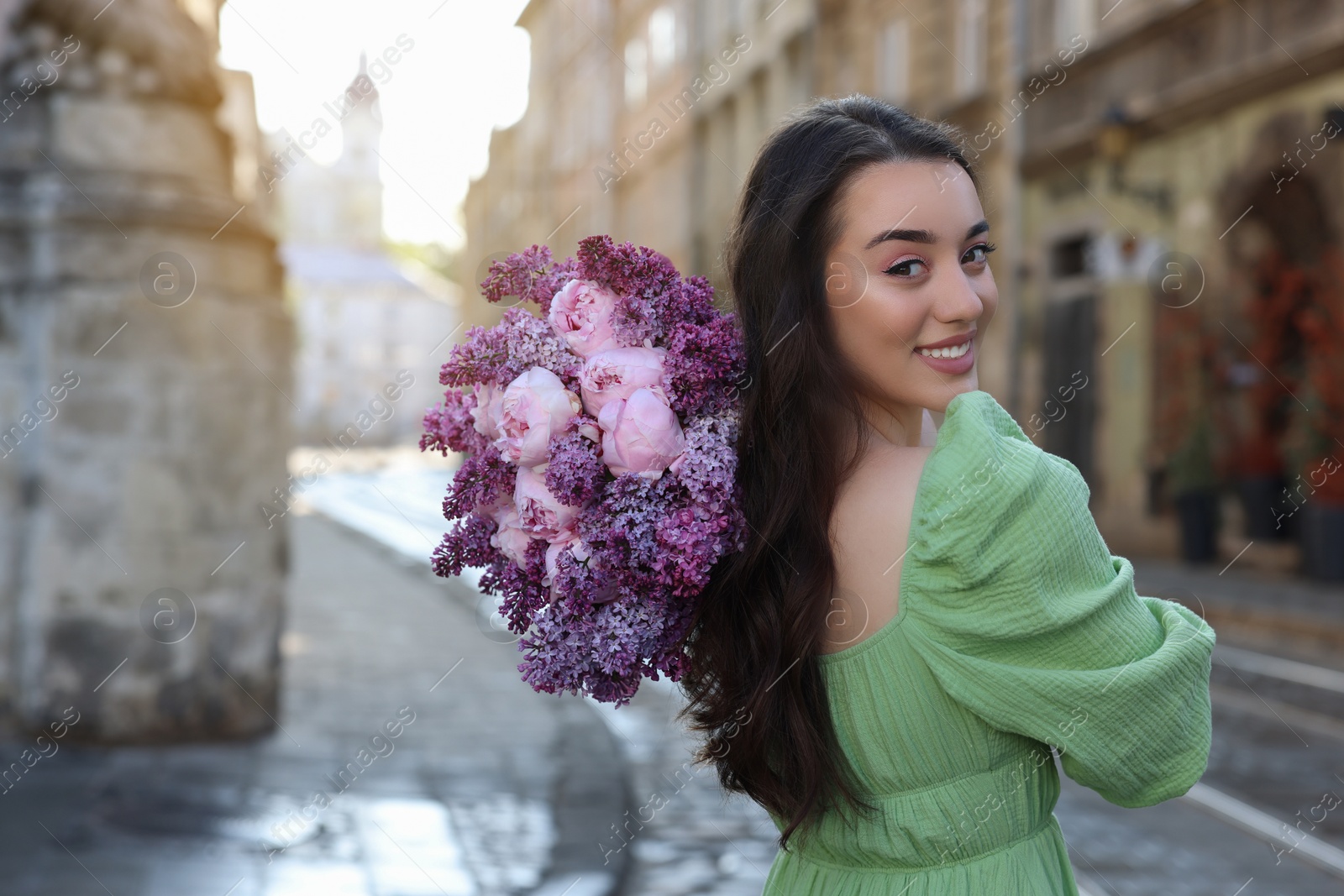 Photo of Beautiful woman with bouquet of spring flowers on city street, space for text