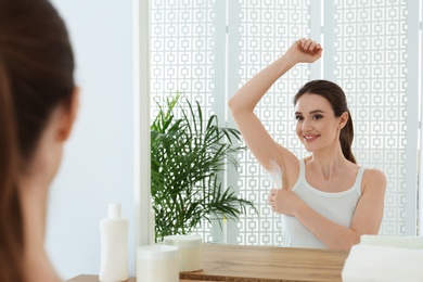 Young woman touching armpit with feather near mirror at home. Epilation procedure