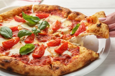 Woman taking piece of delicious Margherita pizza at white table, closeup