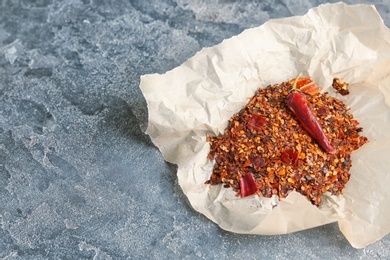 Photo of Parchment with crushed chili pepper and pod on grey background