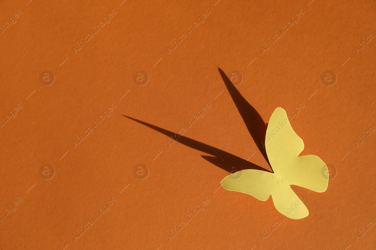 Photo of Yellow paper butterfly on orange background, top view. Space for text