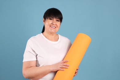 Photo of Happy overweight mature woman with yoga mat on light blue background