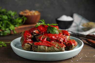 Plate of delicious stuffed grape leaves with tomato sauce and parsley on wooden table, closeup