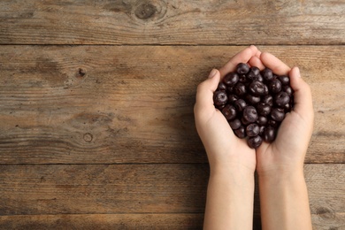 Photo of Top view of woman holding fresh acai berries on wooden background, closeup. Space for text