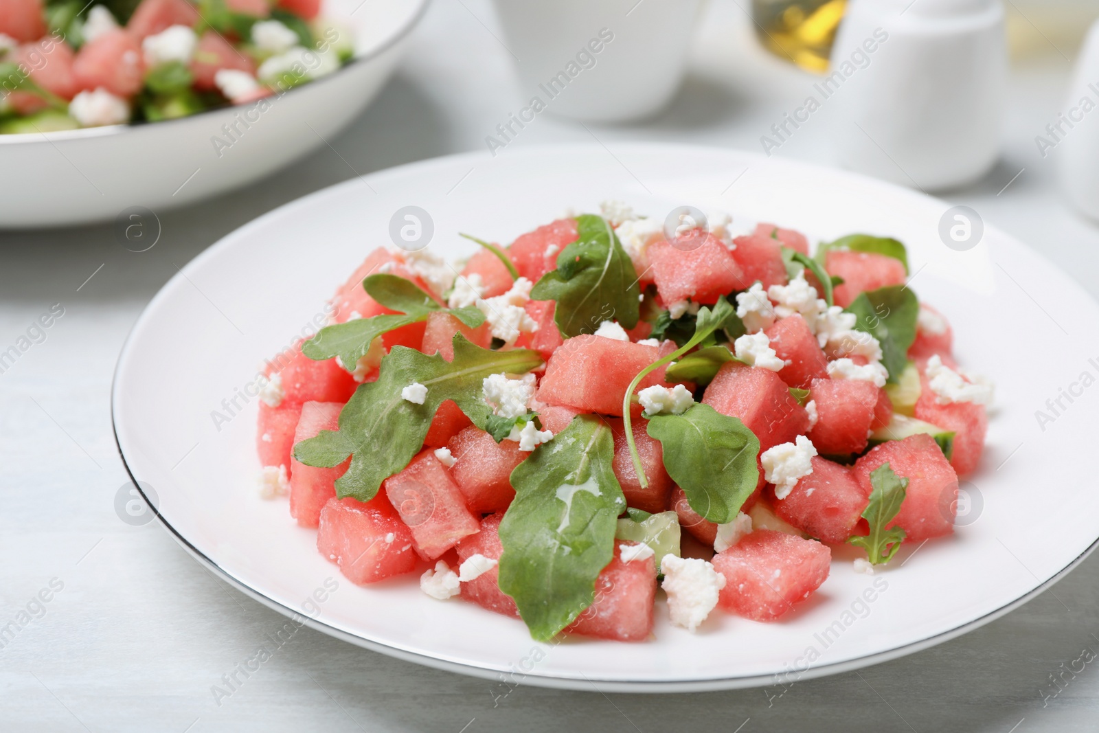 Photo of Delicious salad with watermelon, cucumber, arugula and feta cheese on white wooden table, closeup