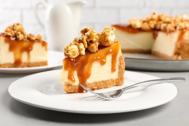 Photo of Piece of delicious caramel cheesecake with popcorn on light grey table, closeup