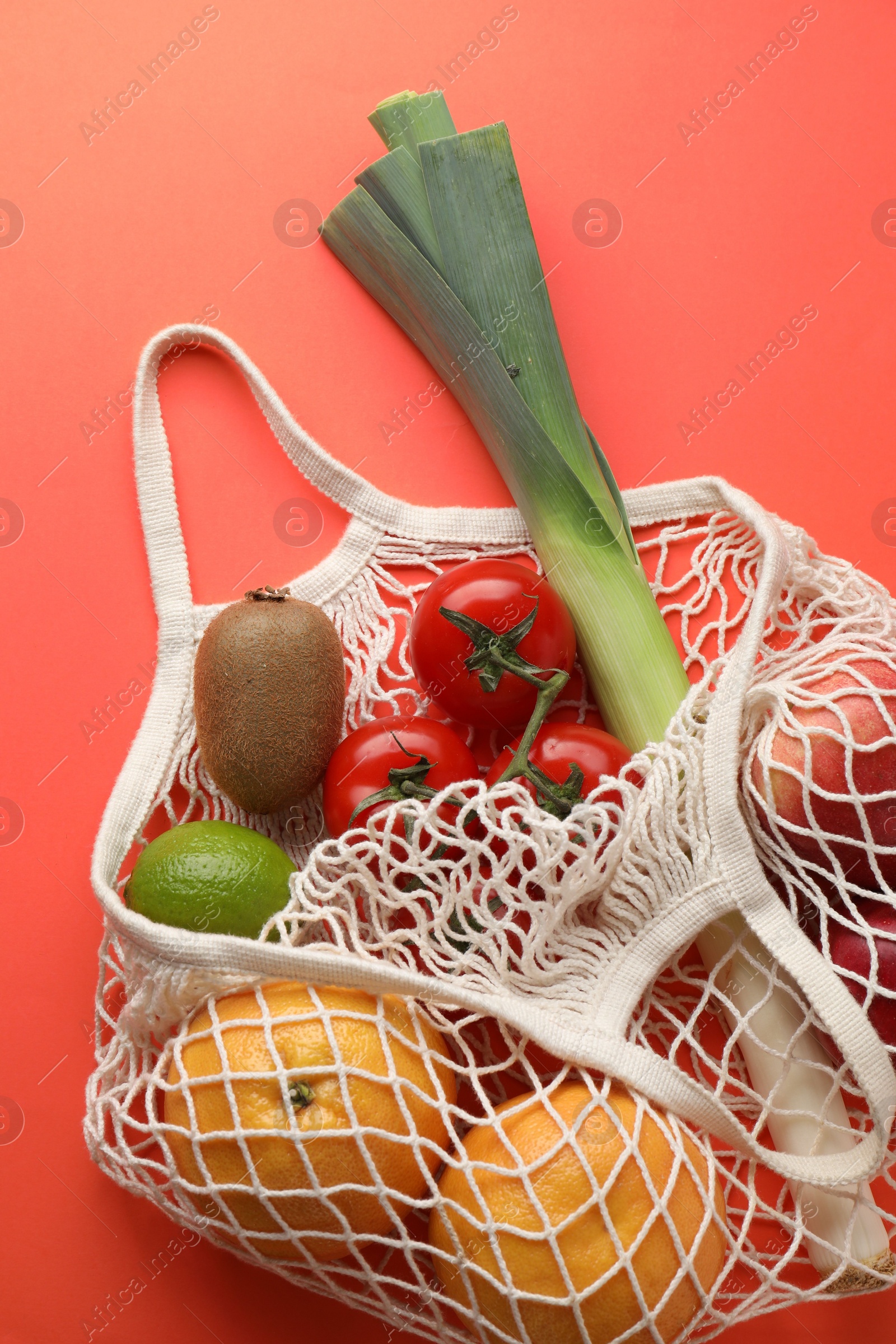 Photo of String bag with different vegetables and fruits on red background, top view