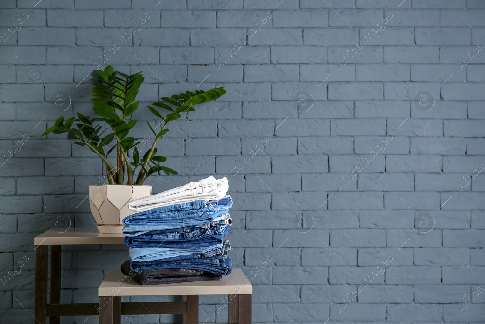 Photo of Stack of different jeans on table against brick wall