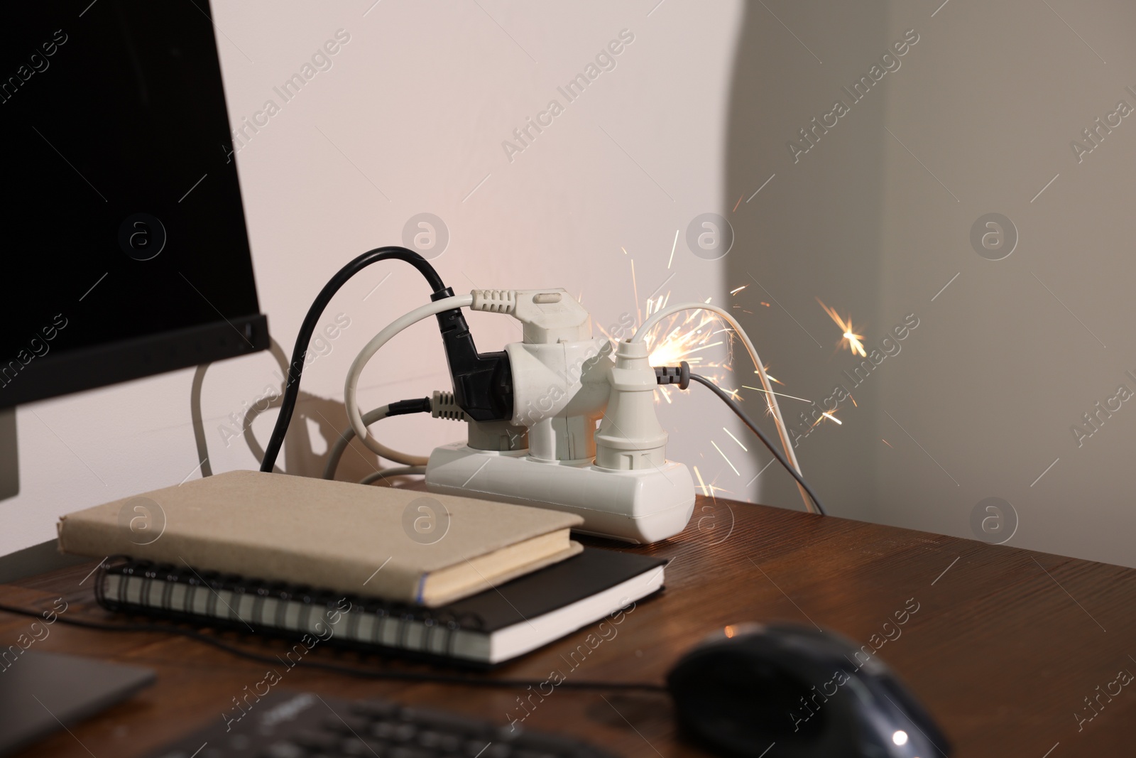 Photo of Inflamed plug in power strip indoors on wooden table. Electrical short circuit