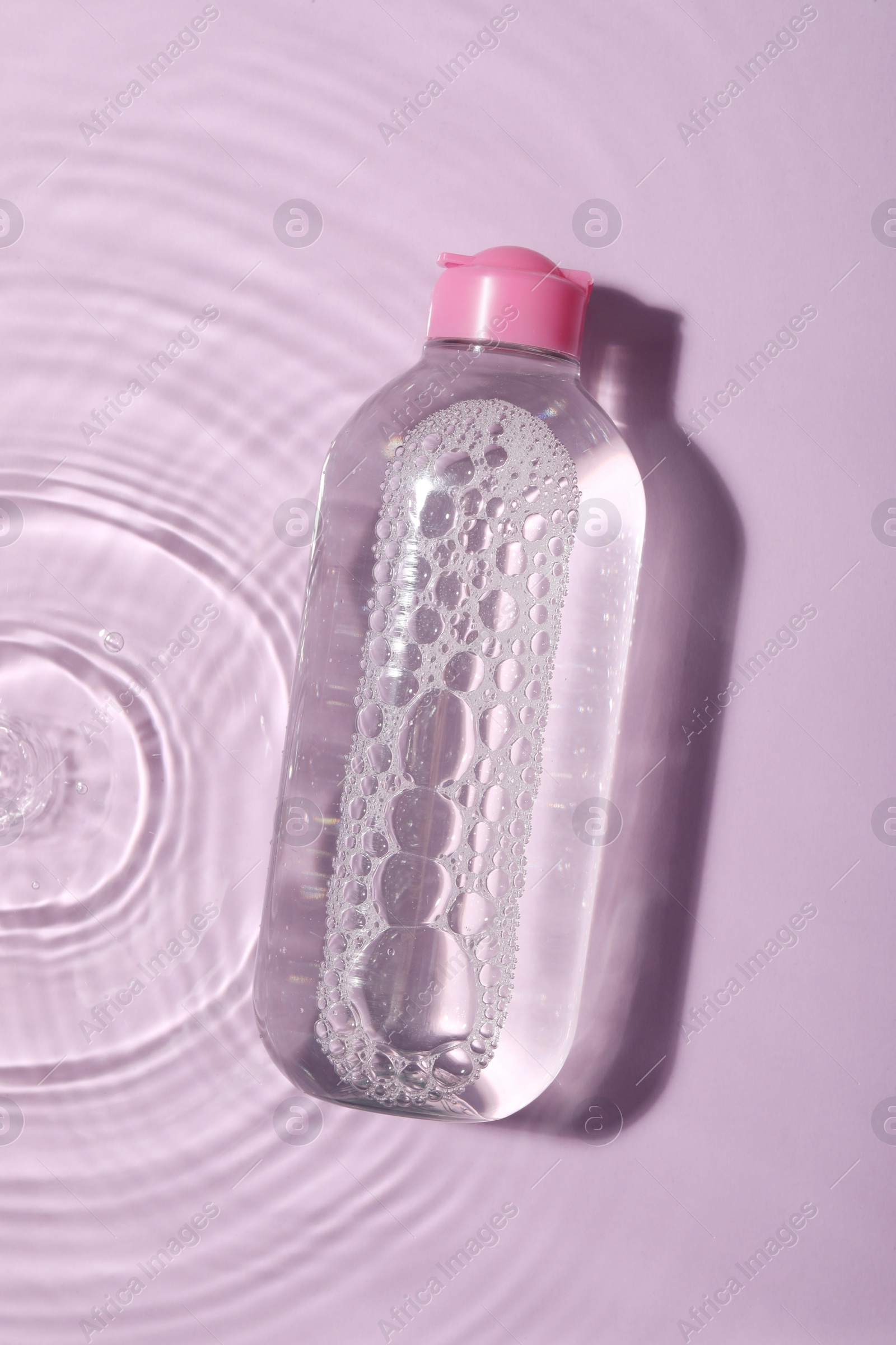 Photo of Wet bottle of micellar water on violet background, top view