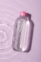 Photo of Wet bottle of micellar water on violet background, top view