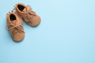 Photo of Brown baby booties on turquoise background, flat lay. Space for text