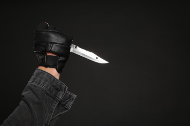 Man holding knife on black background, closeup with space for text. Dangerous criminal