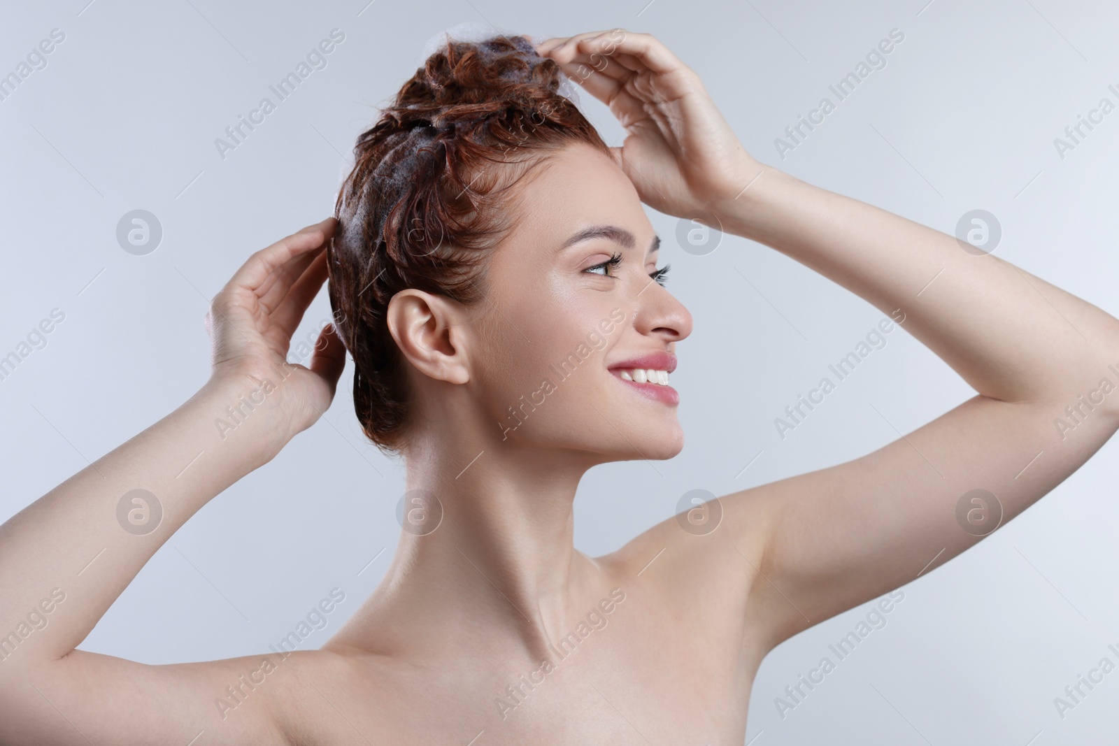 Photo of Happy young woman washing her hair with shampoo on light grey background