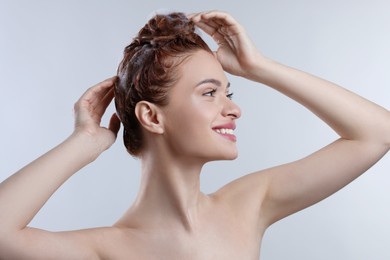 Happy young woman washing her hair with shampoo on light grey background