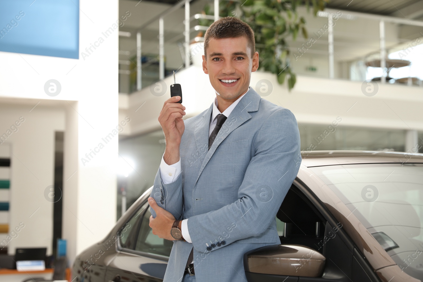 Photo of Young salesman with key near car in modern dealership