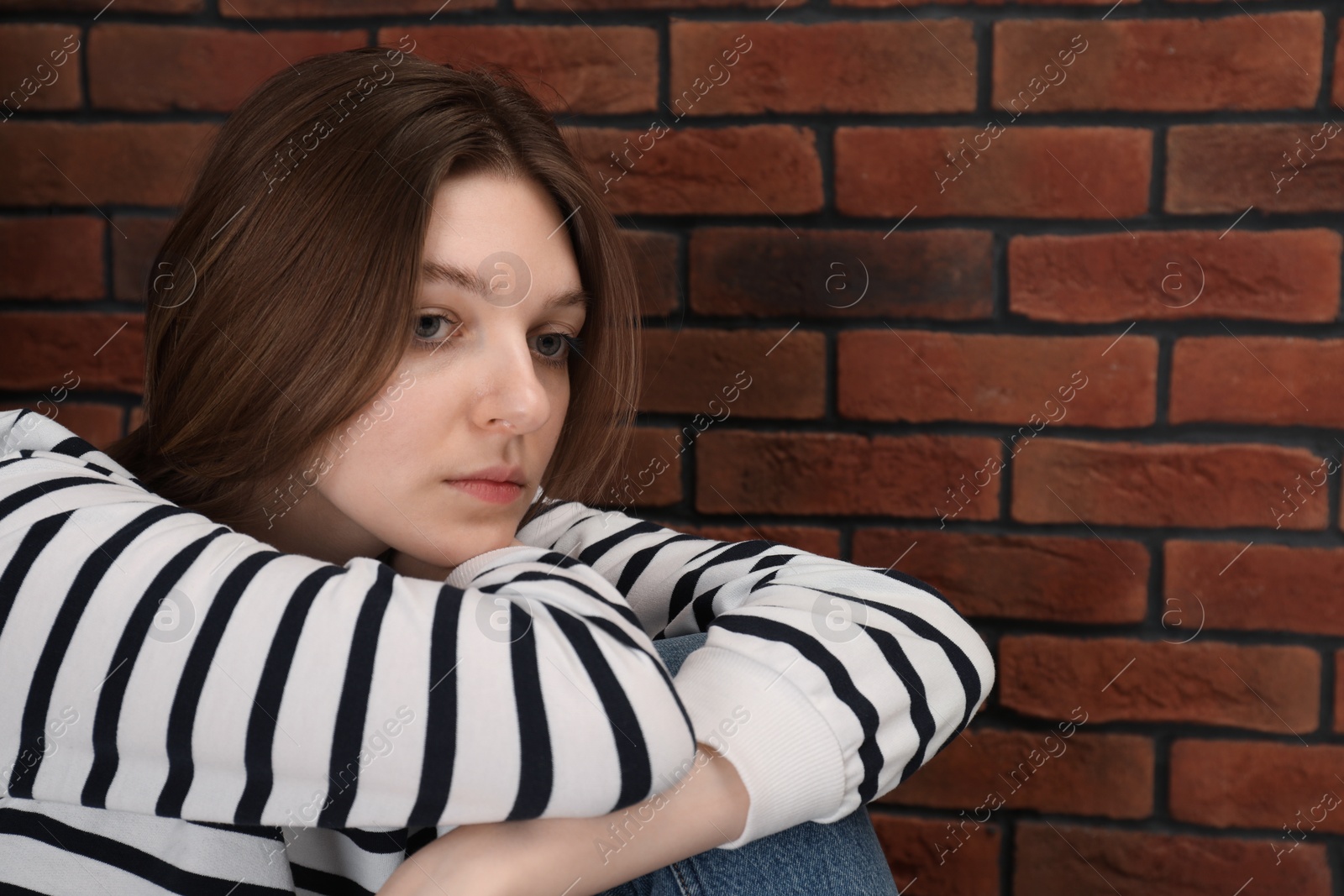 Photo of Sad young woman near brick wall, space for text