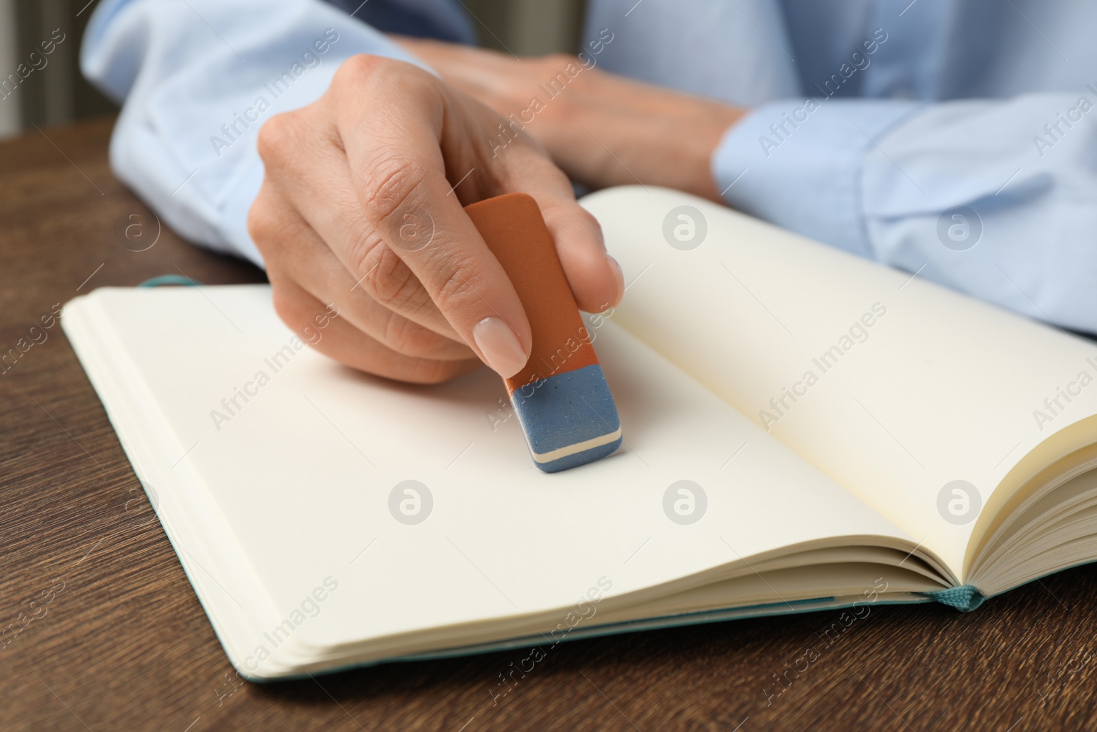 Photo of Woman erasing something in notebook at wooden table, closeup