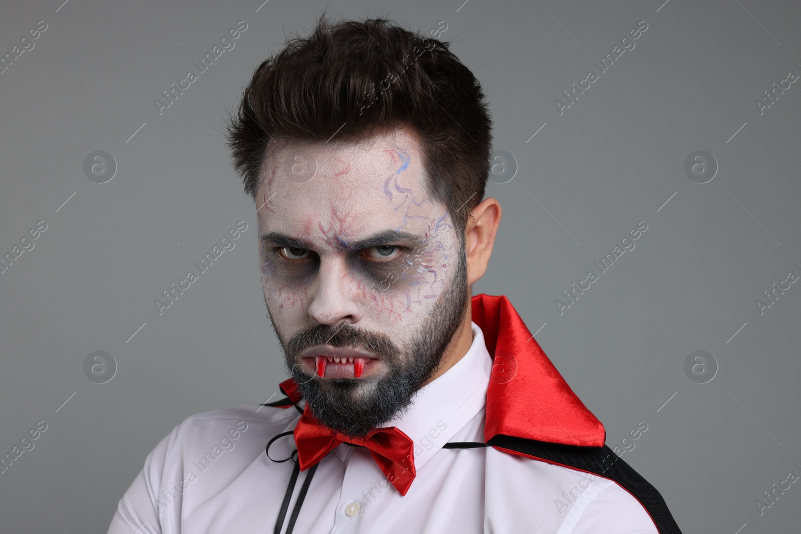 Photo of Man in scary vampire costume with fangs on light grey background. Halloween celebration