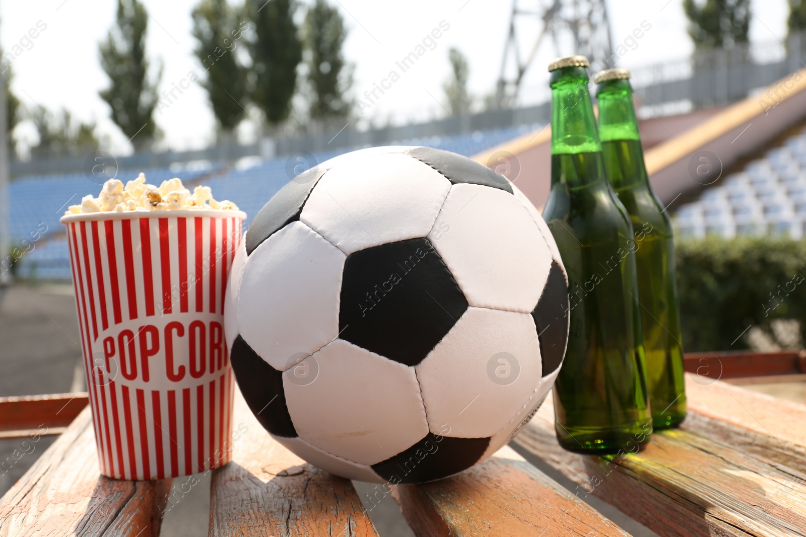 Photo of Football ball with beer and popcorn on wooden bench in stadium