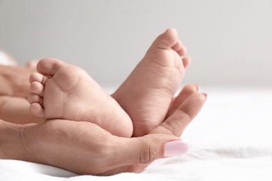 Photo of Mother holding her baby's feet on bed against light background, closeup. Space for text