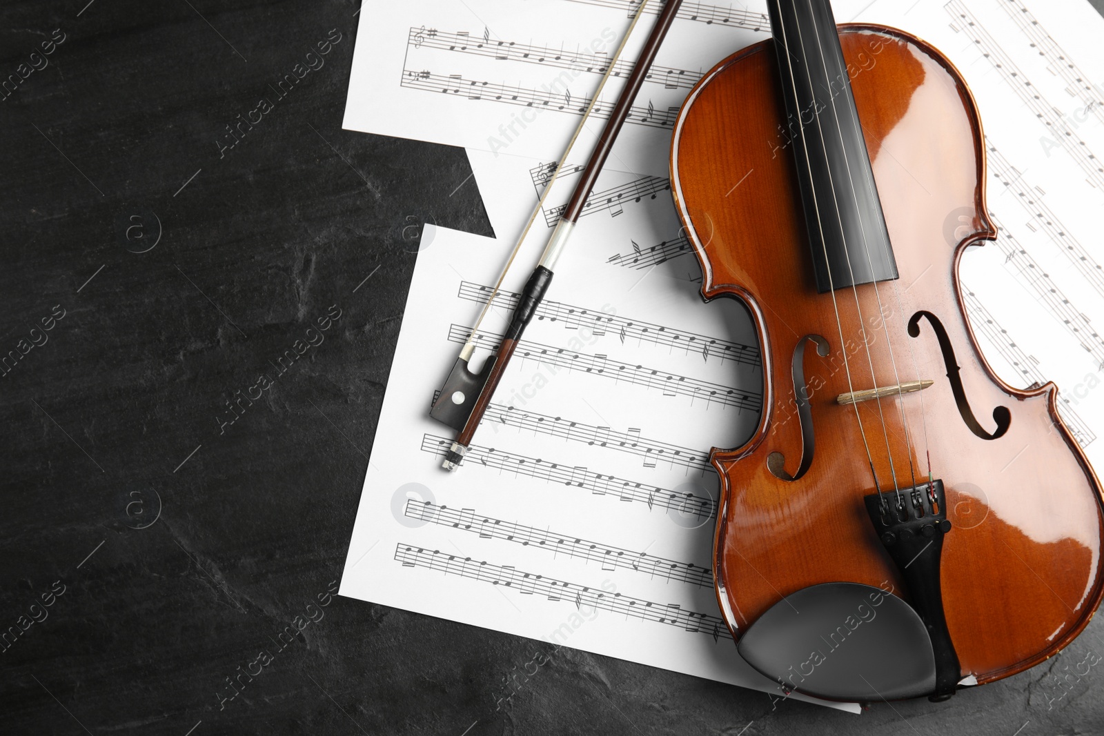 Photo of Violin, bow and note sheets on stone table, flat lay