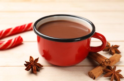 Photo of Tasty hot chocolate, candy cane and spices on light wooden table, closeup