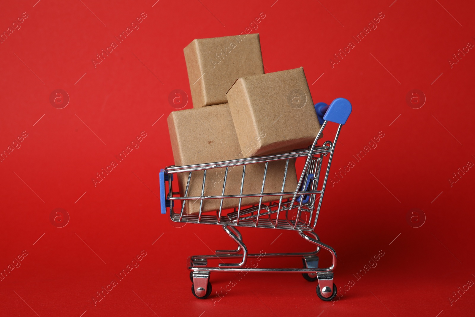Photo of Shopping cart with boxes on red background. Logistics and wholesale concept
