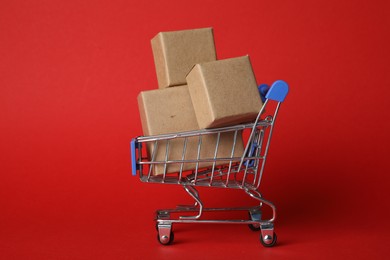 Shopping cart with boxes on red background. Logistics and wholesale concept