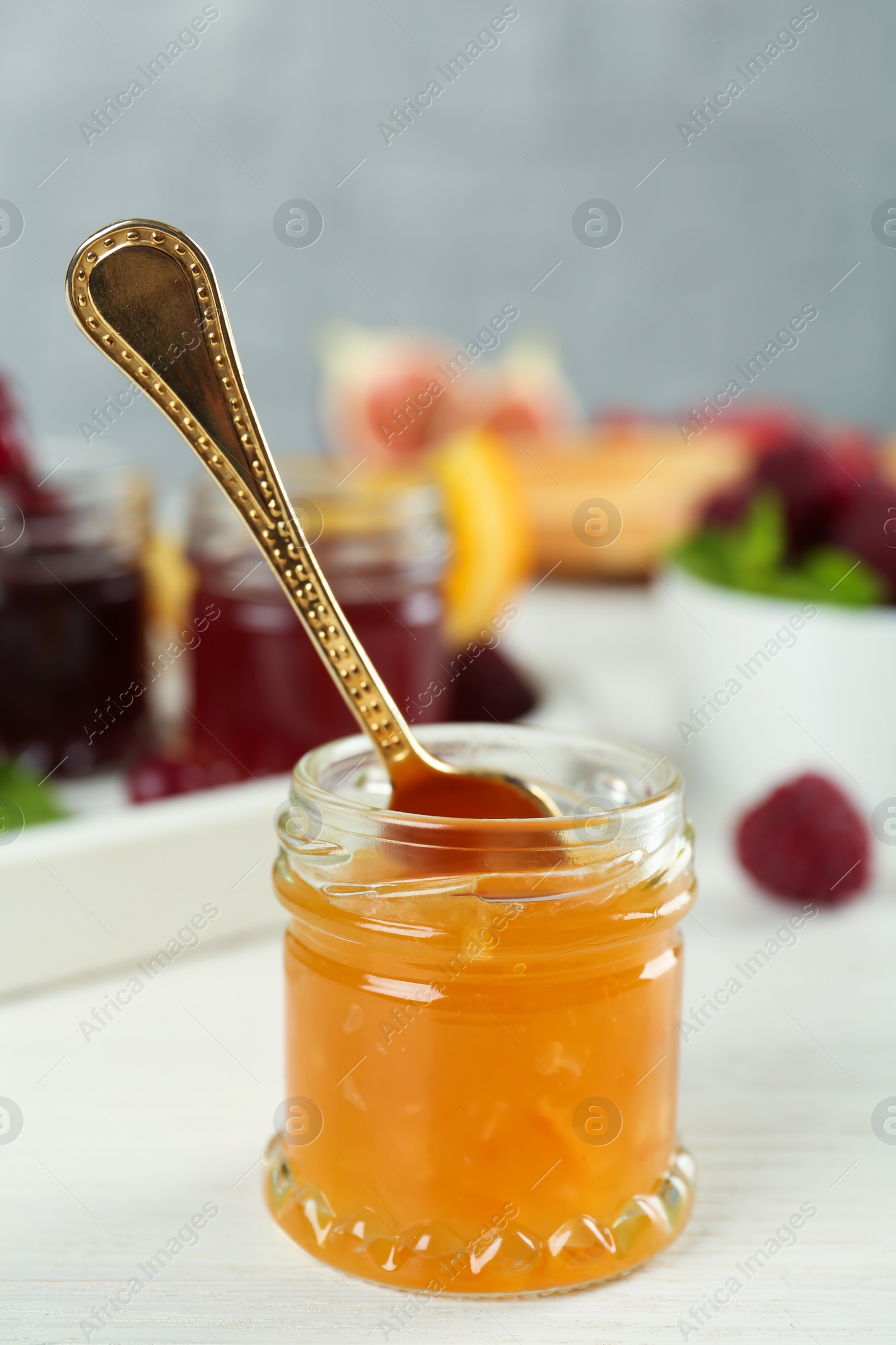 Photo of Open glass jar of sweet jam with spoon on white wooden table