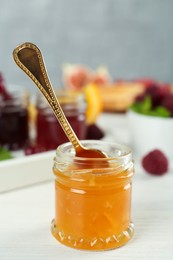 Open glass jar of sweet jam with spoon on white wooden table