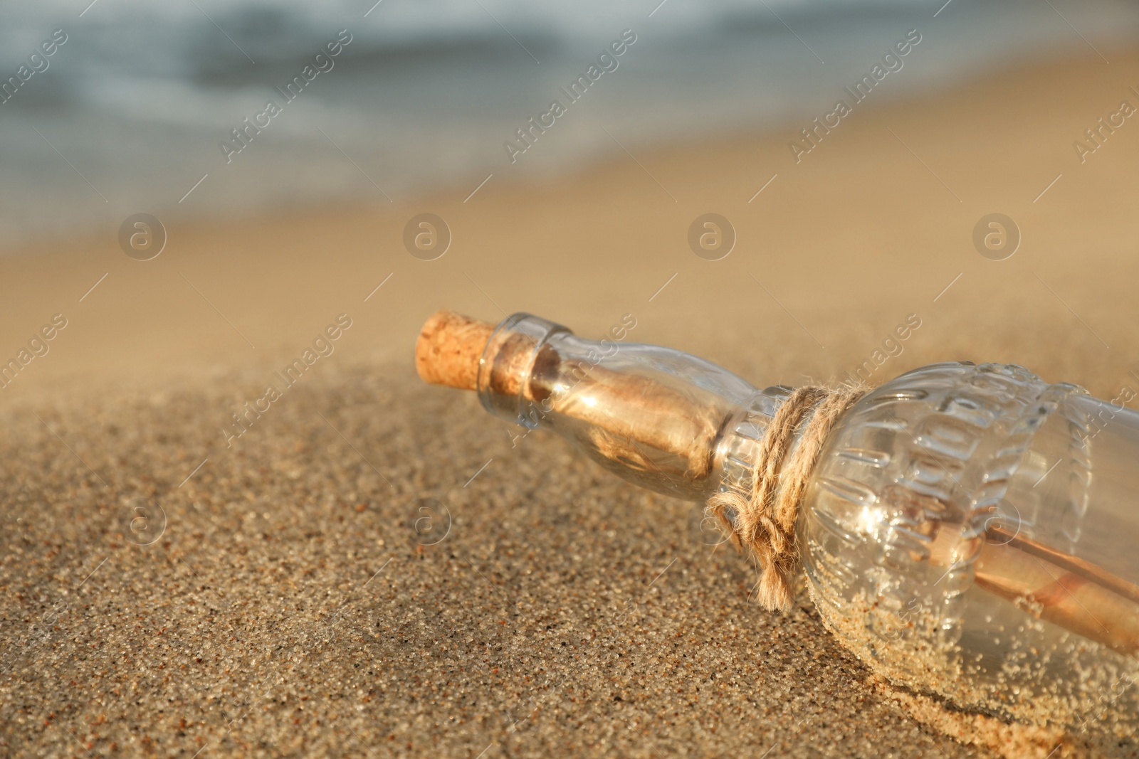 Photo of SOS message in glass bottle on sand, closeup